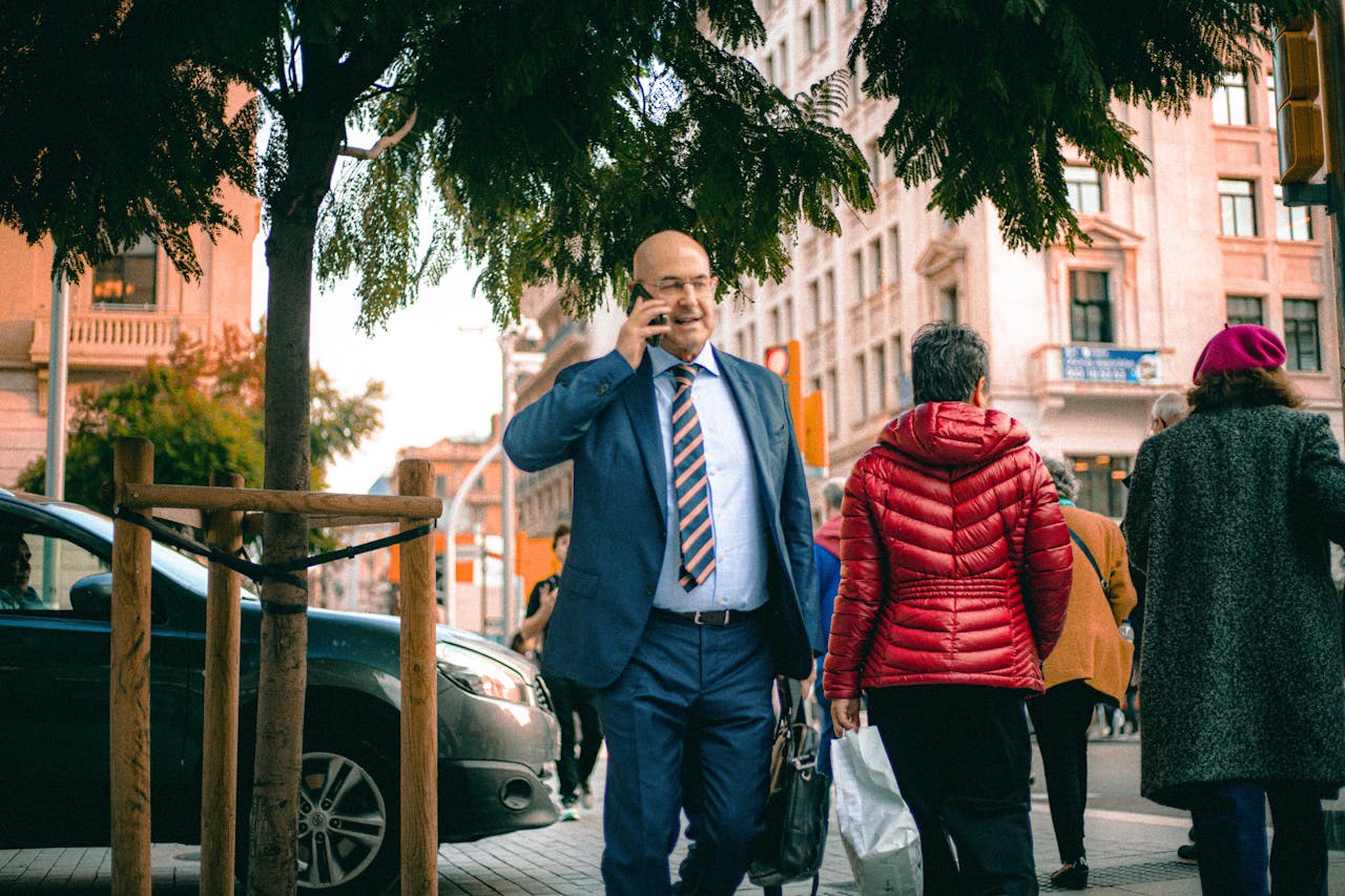 Businessman in a blue suit walking on a bustling city street while talking on his phone.